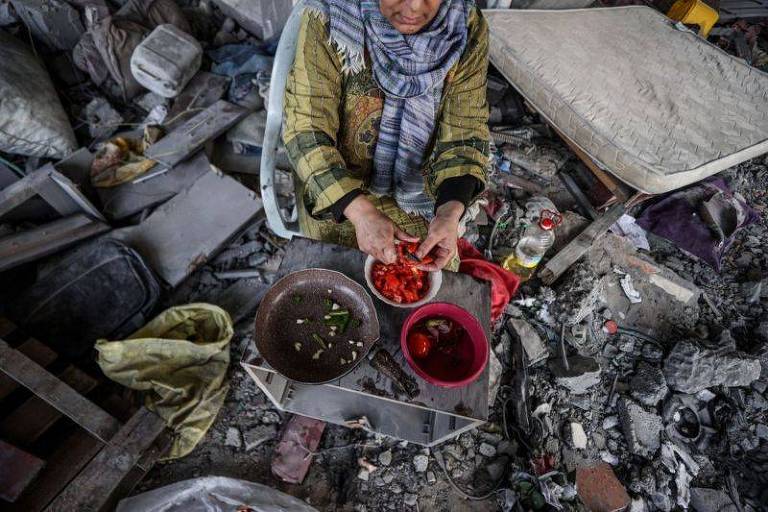 Haleed Naci e sua família preparam alimentos entre os destroços de sua casa destruída por ataques israelenses em Deir al Balah, Gaza