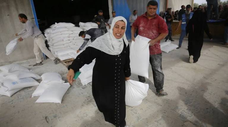 Mulher recolhe um saco de farinha no campo de refugiados de Nuseirat em Deir Al Balah, Gaza.