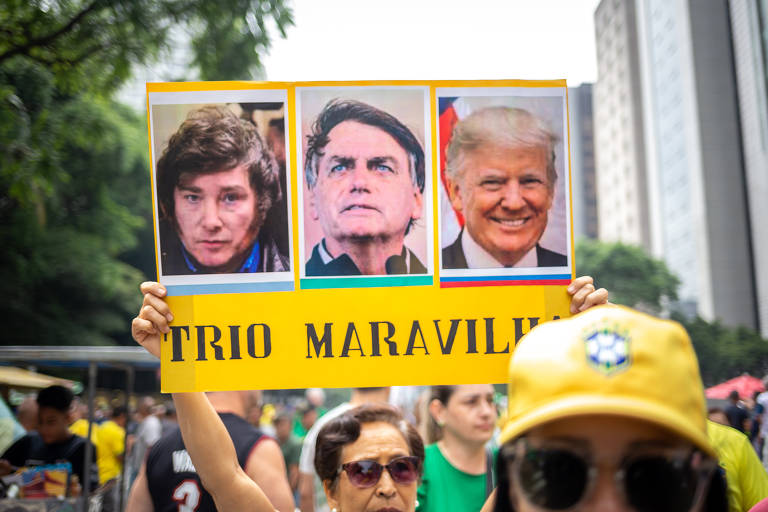 Manifestante exibe cartaz com fotos de Javier Milei, Jair Bolsonaro e Donald Trump em protesto contra a morte de Cleriston Pereira, 46, preso pelos ataques de 8 de janeiro