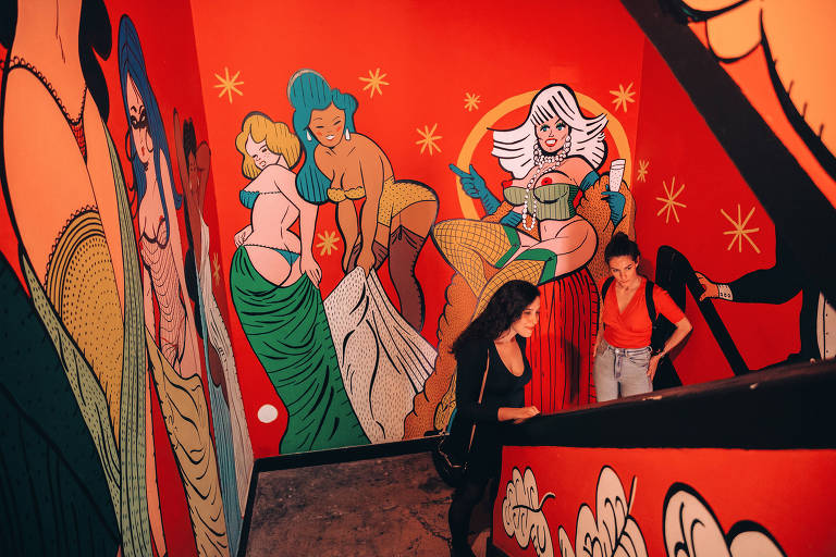 Paredes do prédio do hotel são decoradas com pinturas do ilustrador português Nuno Saraiva. Imagem mostra uma das paredes, com desenhos coloridos de mulheres com pouca roupa. Há duas turistas no canto da foto