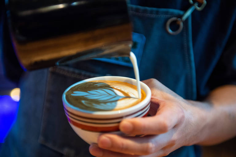 Pessoa serve um cappuccino fazendo desenho com leite sobre um café espresso