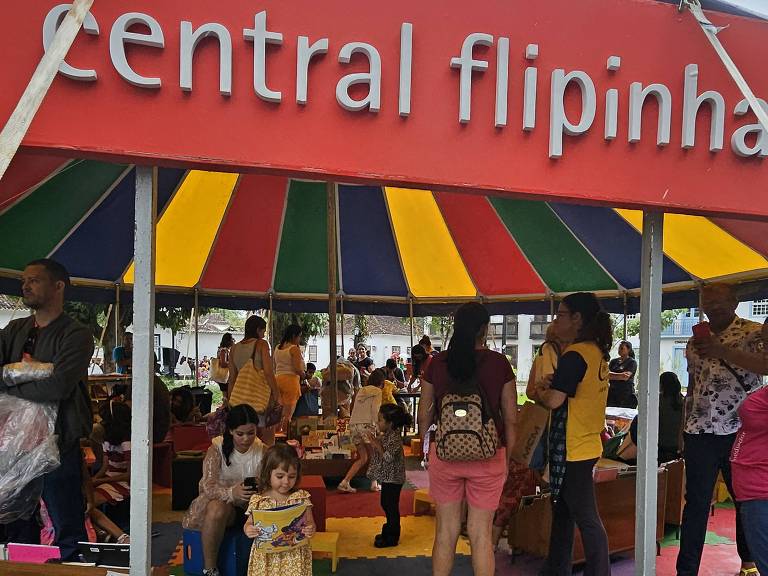 Pessoas na tenda da central flipinha em Paraty. À frente, criança com vestido amarelo segura livro