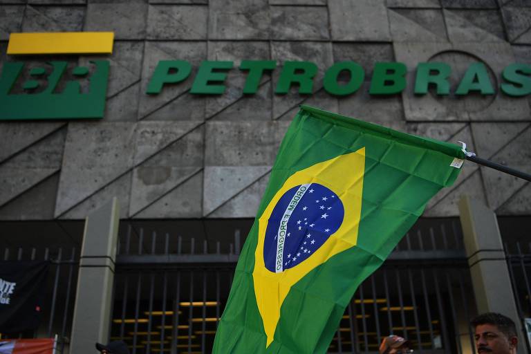 fachada de prédio cinza em que se lê em verde Petrobras, com uma bandeira do Brasil em frente