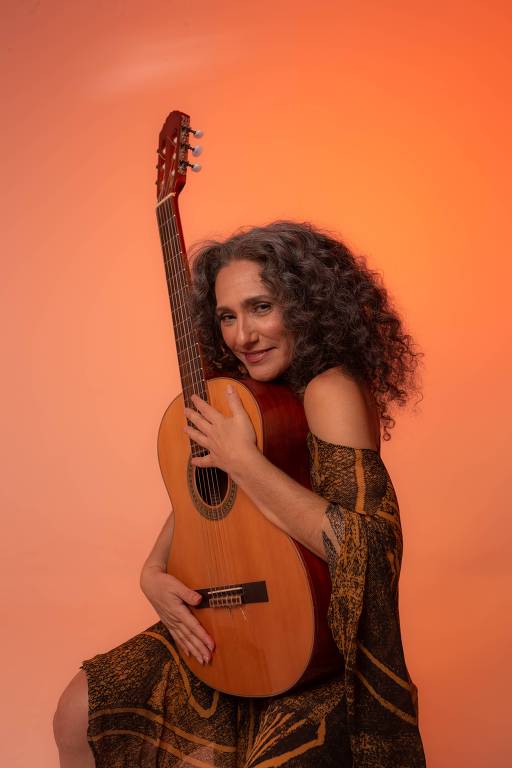 Em foto colorida, a cantora e compositora Badi Assad posa para a câmera com seu violão