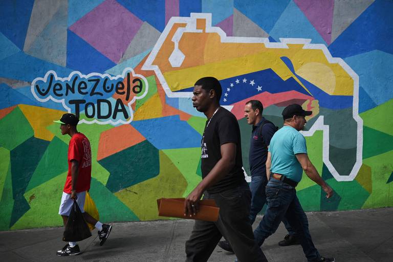 Venezuelanos passam por mural com propaganda do governo sobre o plebiscito, com um mapa mostrando Essequibo já incorporado ao território do país, em Caracas
