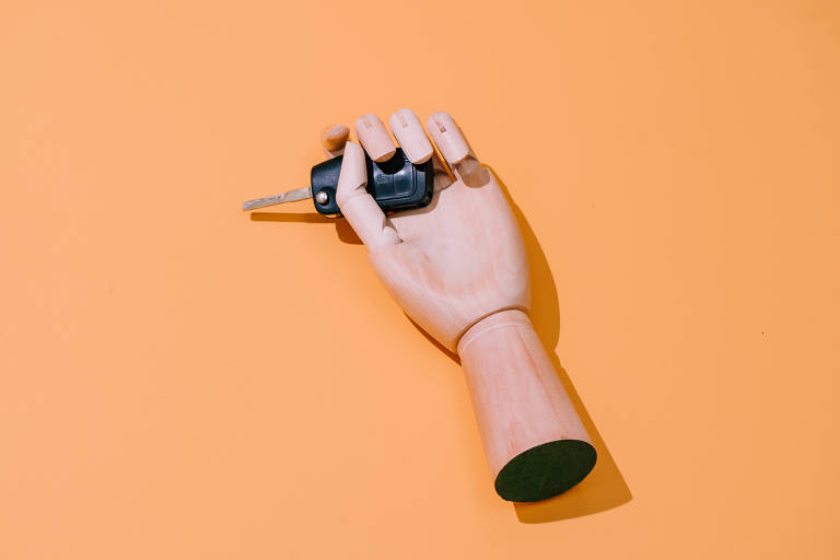 Mão de madeira segurando uma chave de carro sobre um fundo laranja