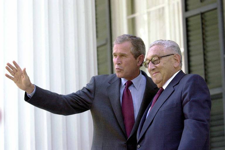 Bush aponta, como se indicasse algo na distância para Kissinger