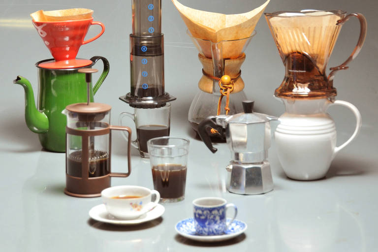 Vários utensílios para preparo de café, como coadores, prensas francesas e cafeteiras italianas sobre uma mesa
