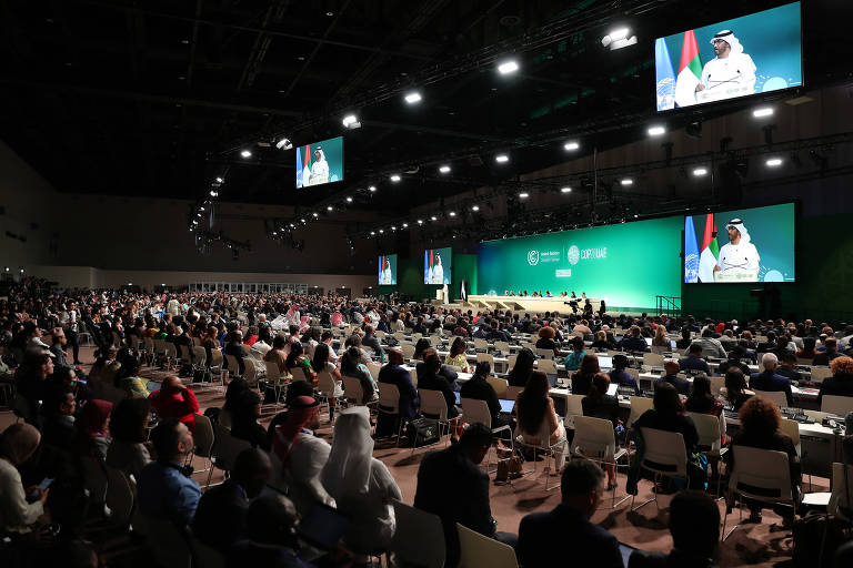 Pessoas em um auditório; no telão aparece Jaber, presidente da COP28