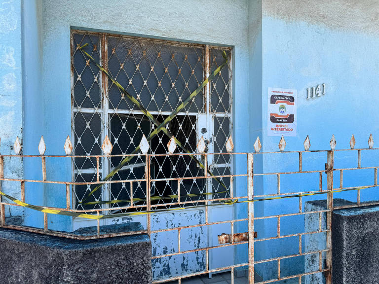 faixa de interdição posta em X em janela de casa azul fechada com portão branco