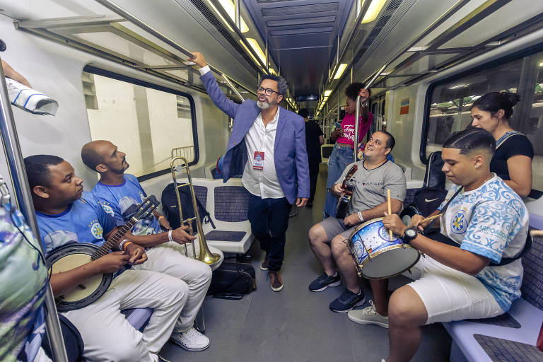 Em foto colorida, o sambista Marquinhos de Oswaldo Cruz aparece com seu grupo tocando samba dentro de um vagão de trem
