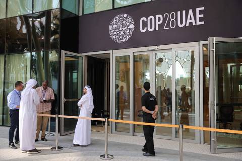 People wait outside a building adroned with a COP28 logo ahead of the United Nations climate summit in Dubai on November 28, 2023. The UN chief urged world leaders to take decisive action to tackle ever-worsening climate change when they gather at the COP28 summit in Dubai starting this week. (Photo by Giuseppe CACACE / AFP)