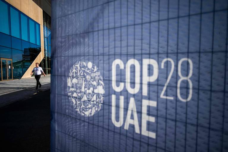 Homem passa perto de placa no local onde é realizada a COP28 em Dubai 