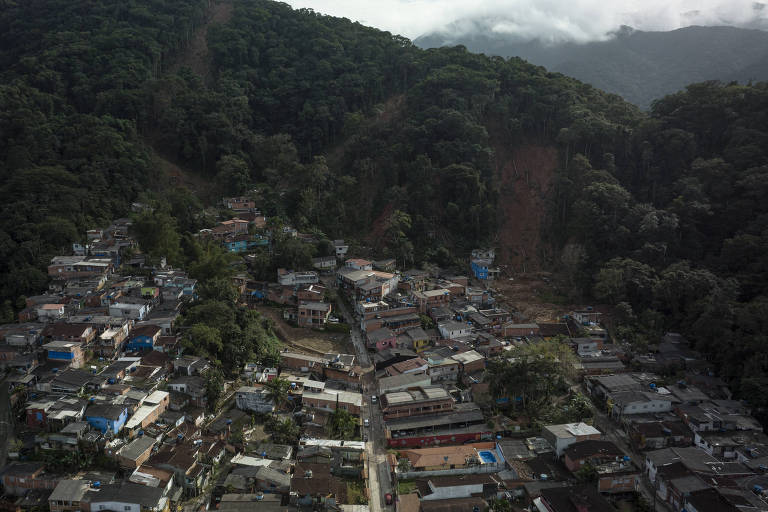 Imagem aérea mostra o bairro repleto de pequenas casas no sopé da montanha, que ainda possui áreas de mata devastadas pelos desmoronamentos