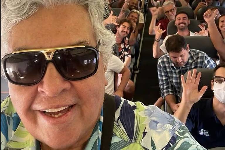Em foto colorida, homem de óculos escuros faz foto dentro de um avião com vários fãs