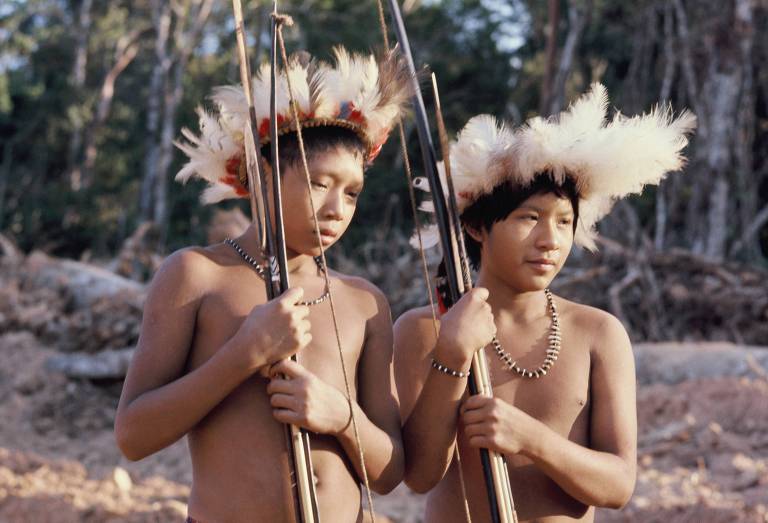 dois jovens da etnia indígena cinta-larga fotografados, usam cocar e seguram arcos e algumas flechas
