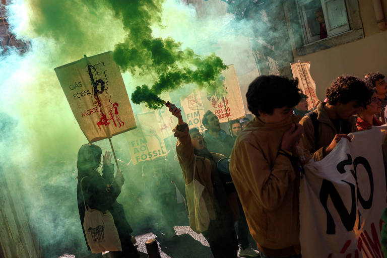 Jovens levam cartazes e faixas em meio a uma fumaça verde