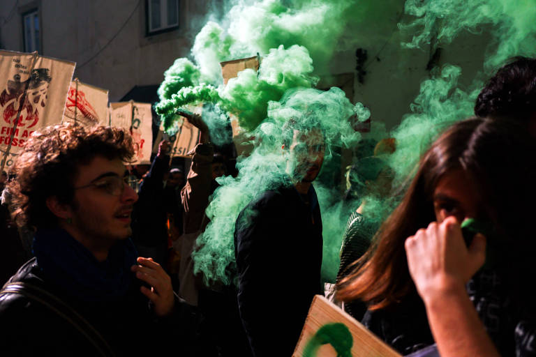 Jovens em meio a uma fumaça verde e cartazes no meio de uma rua à noite