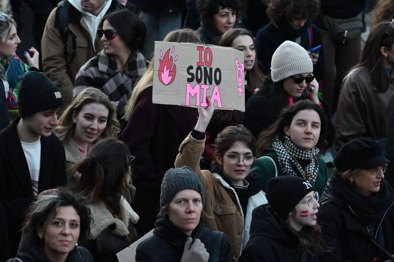 Mulher jovem branca segura cartaz com a frase "Eu sou minha" (Io sono mia, em italiano) em meio a multidão durante protesto contra violência contra mulheres em Roma