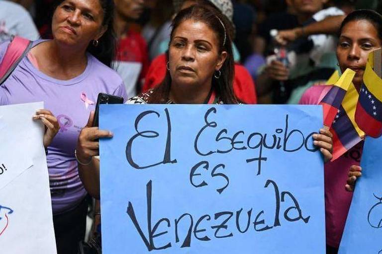 Manifestantes venezuelanos seguram cartazes de apoio ao referendo que trata sobre anexação de território da Guiana