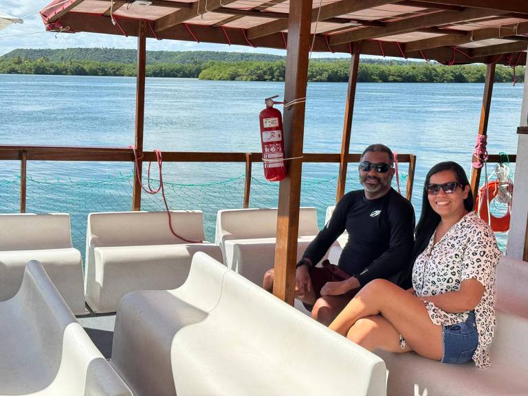 casal posa sentados em banco dentro de barco em lago