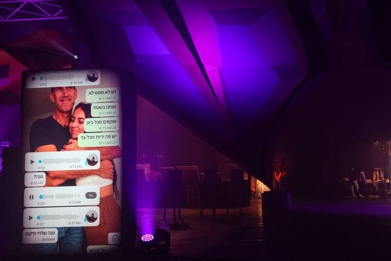 Telão imitando smartphone na exposição '06h29', em Tel Aviv, exibe mensagens de WhatsApp escritas por vítimas de ataque do Hamas a rave no deserto de Negev