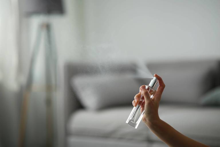 Mão borrifa líquido em frasco transparente em sala com sofá e luminária
