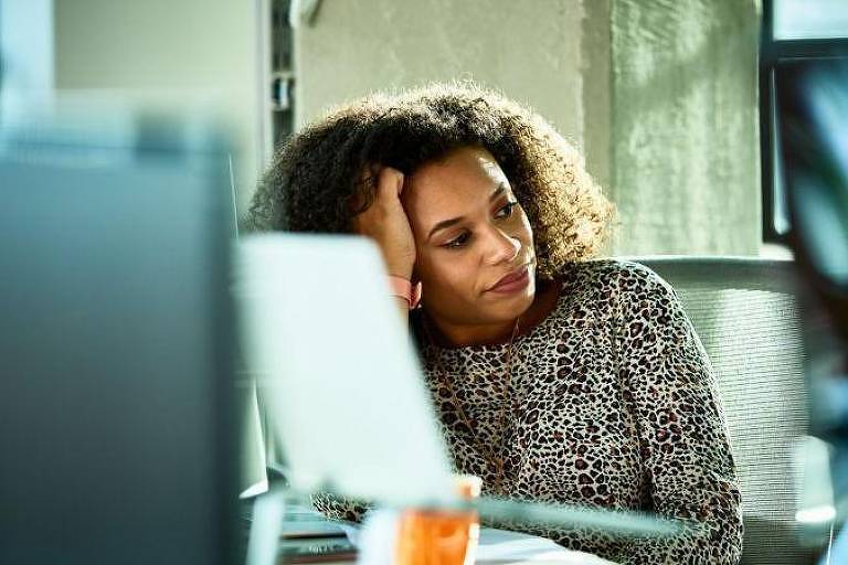 Fotografia mostra uma mulher negra sentada em frente ao computador