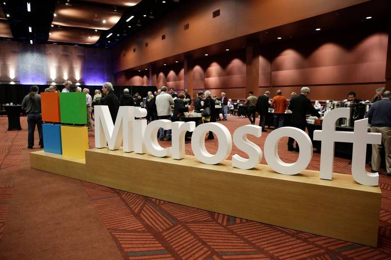 Logotipo branco em que se lê Microsoft, com pessoas ao fundo em uma recepção