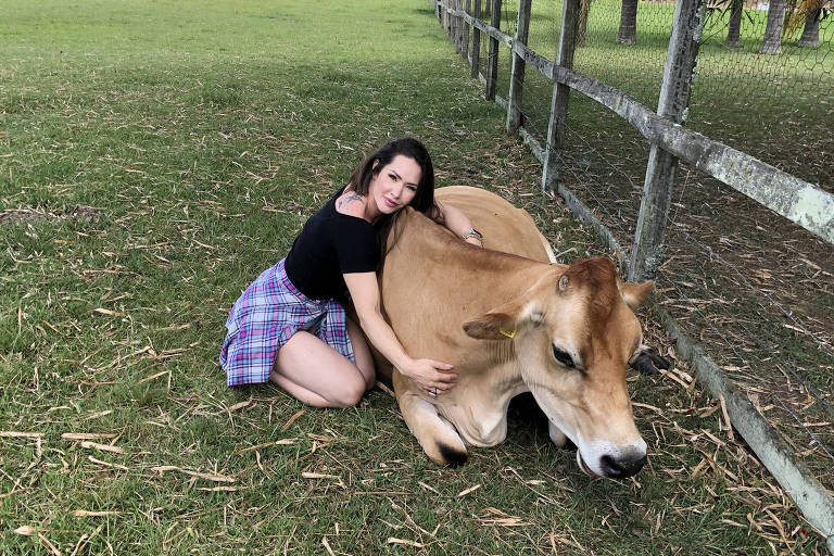 Francielle é uma mulher branca e loira. Ela está em um campo, abraçada com uma vaca de tonalidade caramelo.