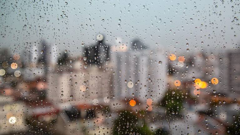 Pingos de chuva sobre janela com cidade ao fundo