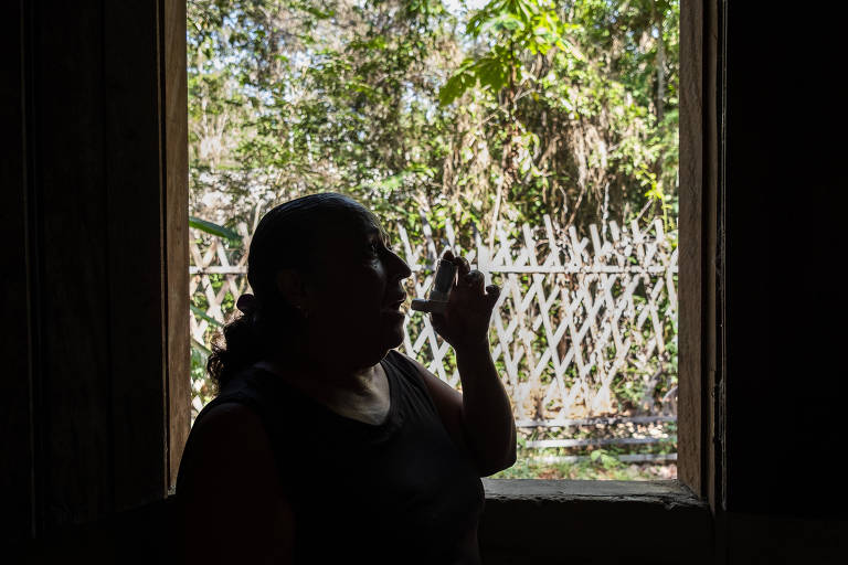 Mulher usa bombinha contra asma em frente a uma janela