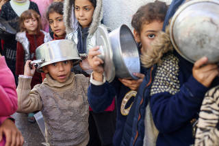 Palestinian children wait to receive food cooked by a charity kitchen, in Rafah