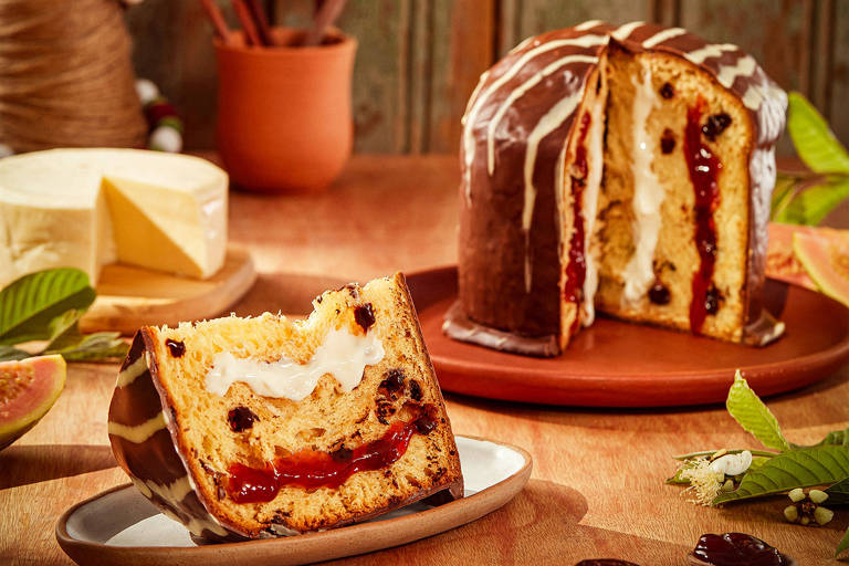 A foto mostra um panetone fatiado com cobertura de chocolate e duplo recheio: goiabada e queijo. Ao fundo, um queijo fatiado e peças de cerâmica