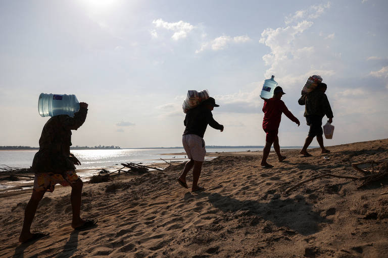 Quatro pessoas carregam galões de água enquanto caminham em leito seco de rio 