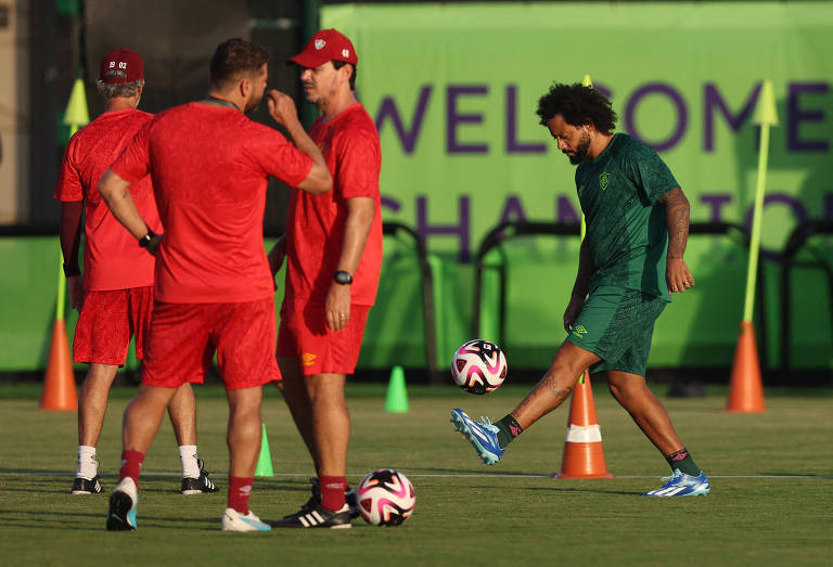 Registro do treino do Fluminense em Jeddah, na Arábia Saudita, mostra Marcelo fazendo embaixadinhas, vestido de verde, e Fernando Diniz e sua comissão técnica ao lado, com uniformes vermelhos