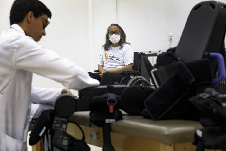 Helena Torres Souza, 70, observa o fisioterapeuta Rafael Francisco Vieira de Melo preparar o exoesqueleto