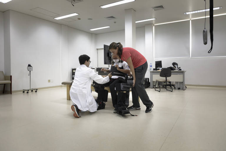 Helena dá o comando ao sensor e, com a ajuda dos fisioterapeutas, fica em pé