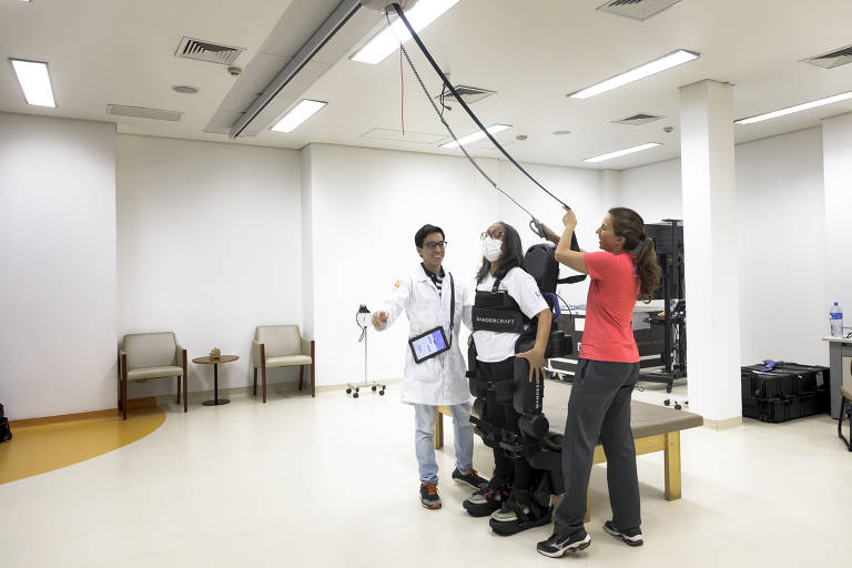 Helena dá o comando ao sensor e, com a ajuda dos fisioterapeutas, fica em pé