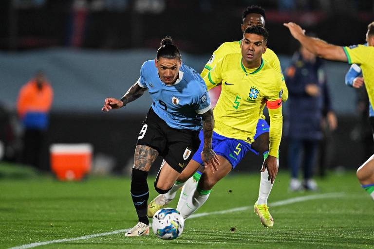 Capitão da seleção brasileira, Casemiro, usando a camisa amarela com o número cinco, tenta acompanhar o uruguaio Darwin Núñez, que usa camisa azul com o númeor nove, em jogo em Montevidéu pelas Eliminatórias da Copa de 2026