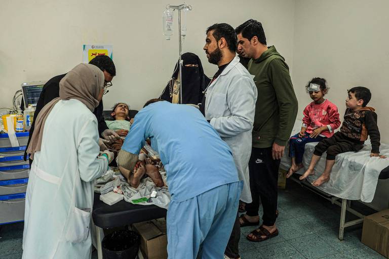 Menina palestina ferida recebe atendimento em hospital após bombardeio de Israel em Rafah, no sul da Faixa de Gaza, ao lado de outras crianças também com machucados pelo corpo