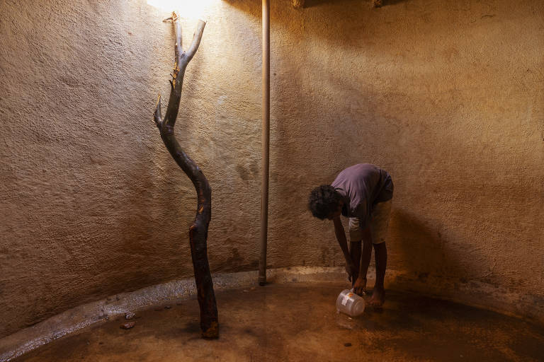 Levi Santos, filho de Maria da Conceição Santos, recolhe o que sobrou da água da cisterna da família com a ajuda de um pote, na comunidade quilombola do Baixão, na zona rural de Betânia do Piauí