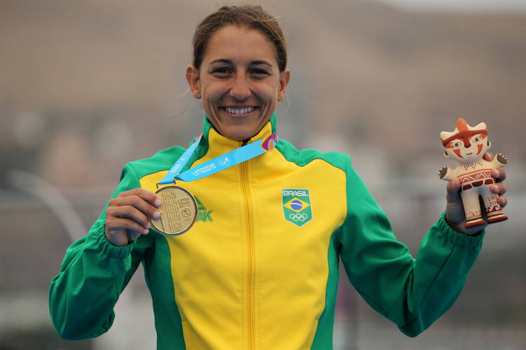 Triatleta brasileira Luisa Baptista, vestida com casaco amarelo, exibe medalha de ouro no Pan de Lima, em 2019