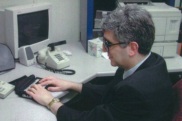 Alan Clive em uma mesa usando terminal braille.