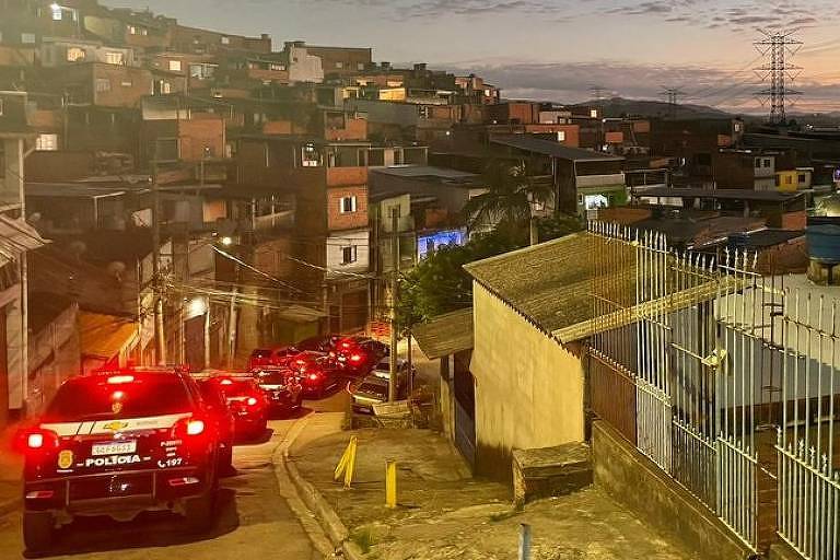viaturas trafegam por viela, favela ao fundo