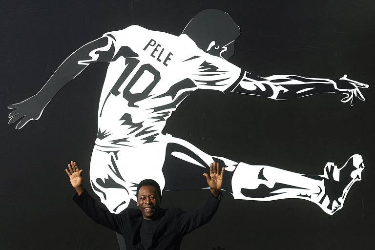 Com os dois braços erguidos e diante de uma imagem sua atuando pelo Santos, Pelé acena na cerimônia de abertura de exposição "As Marcas do Rei", em sua homenagem, em 2008 em Brasília  