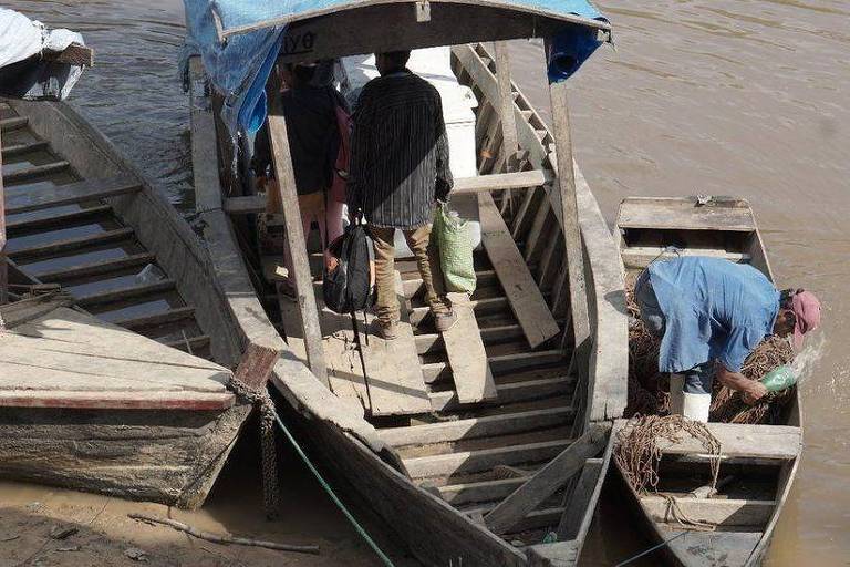 Dois pescadores organizam equipamentos em um barco maior e uma canoa