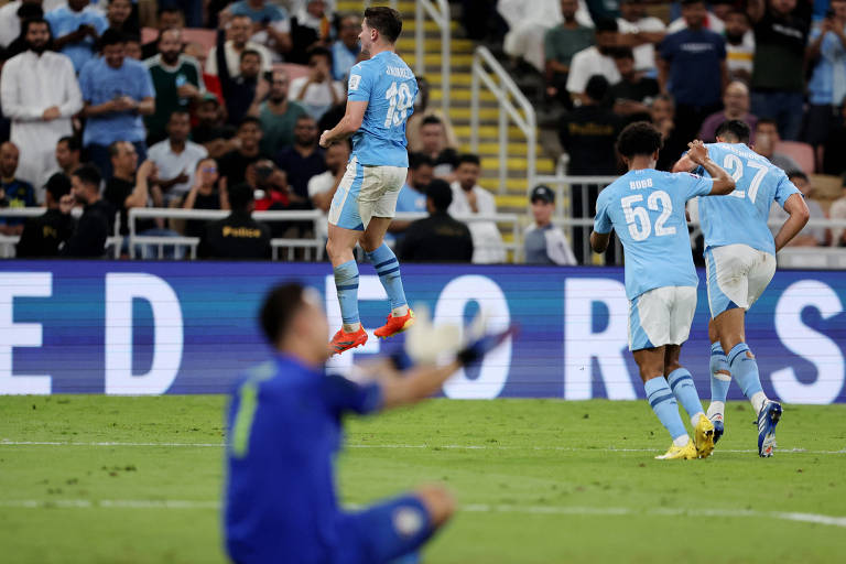 Seguido por dois colegas de time, o argentino Julian Álvarez salta para festejar seu gol, o quarto do Manchester City na goleada sobre o Fluminense na final do Mundial de Clubes, na Arábia Saudita; em primeiro plano, o goleiro Fábio sentado no gramado