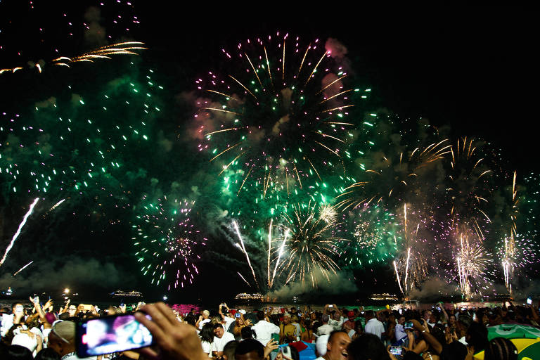 Fogos de artifícios no céu e pessoas acompanham na praia 