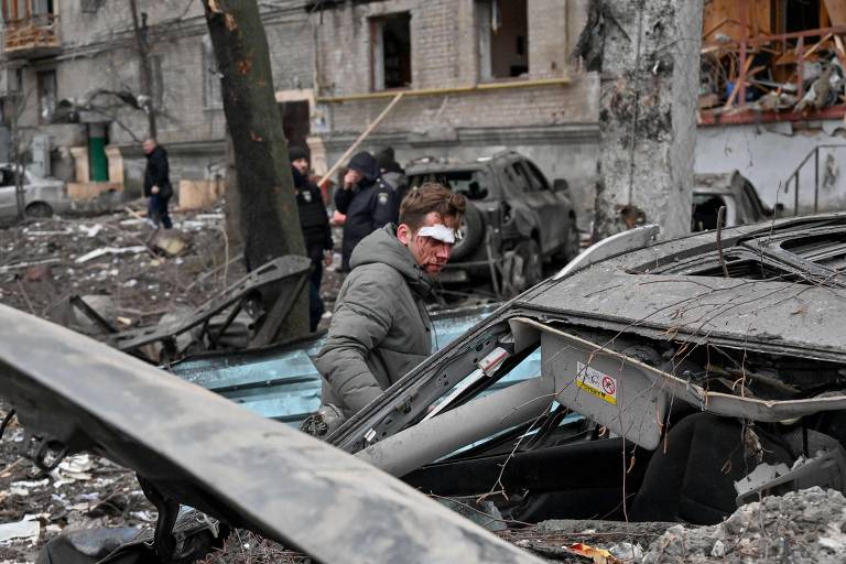Homem ferido examina seu carro destruído no lado de fora de um prédio residencial, no centro de Kharkiv